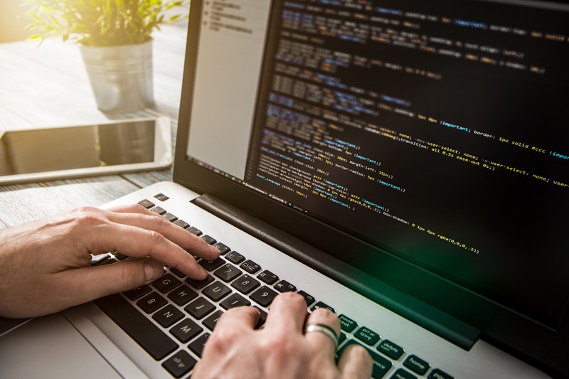 A person types code on a laptop.