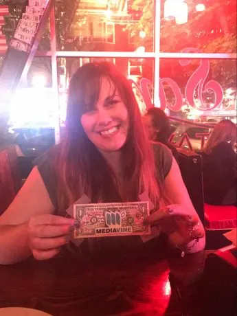 Heather holds up a dollar bill featuring a Mediavine logo sticker.