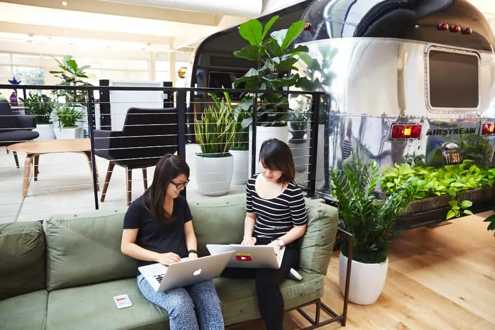 Two female bloggers work on laptops in a coworking space.