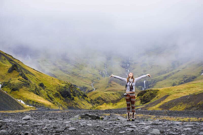 kristin addis looking up with her arms stretched out in front of green landscape