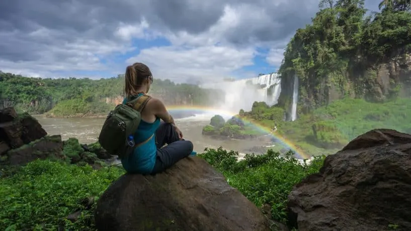 Kristin Addis sits in front of a waterfall, complete with rainbow arcing in front of her.