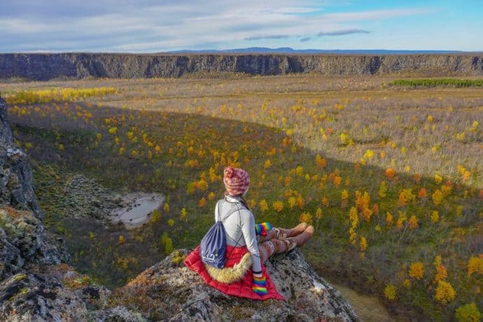 Kristin Addis sits atop a rocky outcrop overlooking a field of flowers.