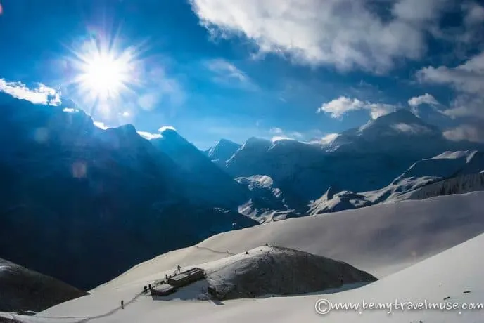 The sun shines over a snowy mountain range.