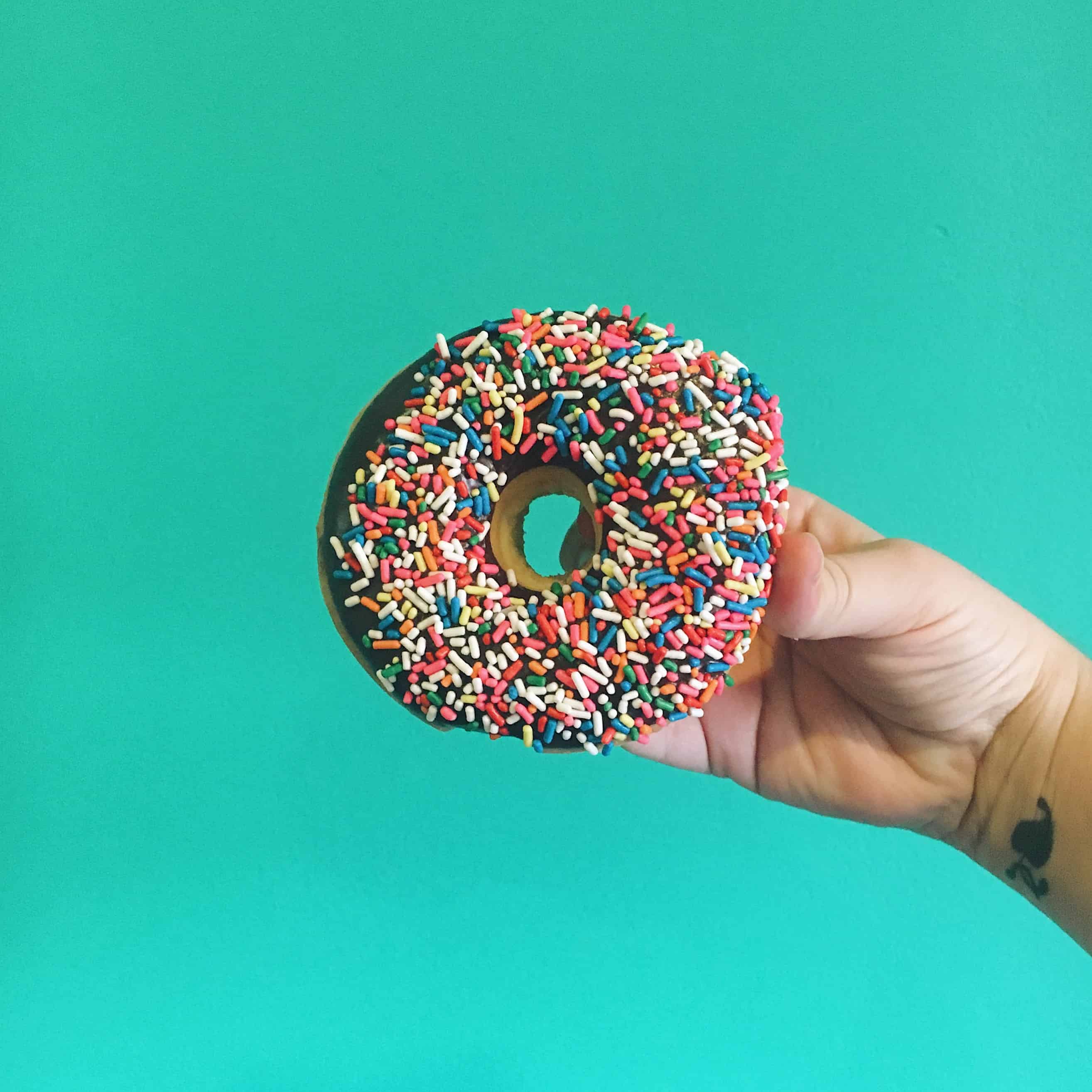 A sprinkle-covered donut against a teal background.