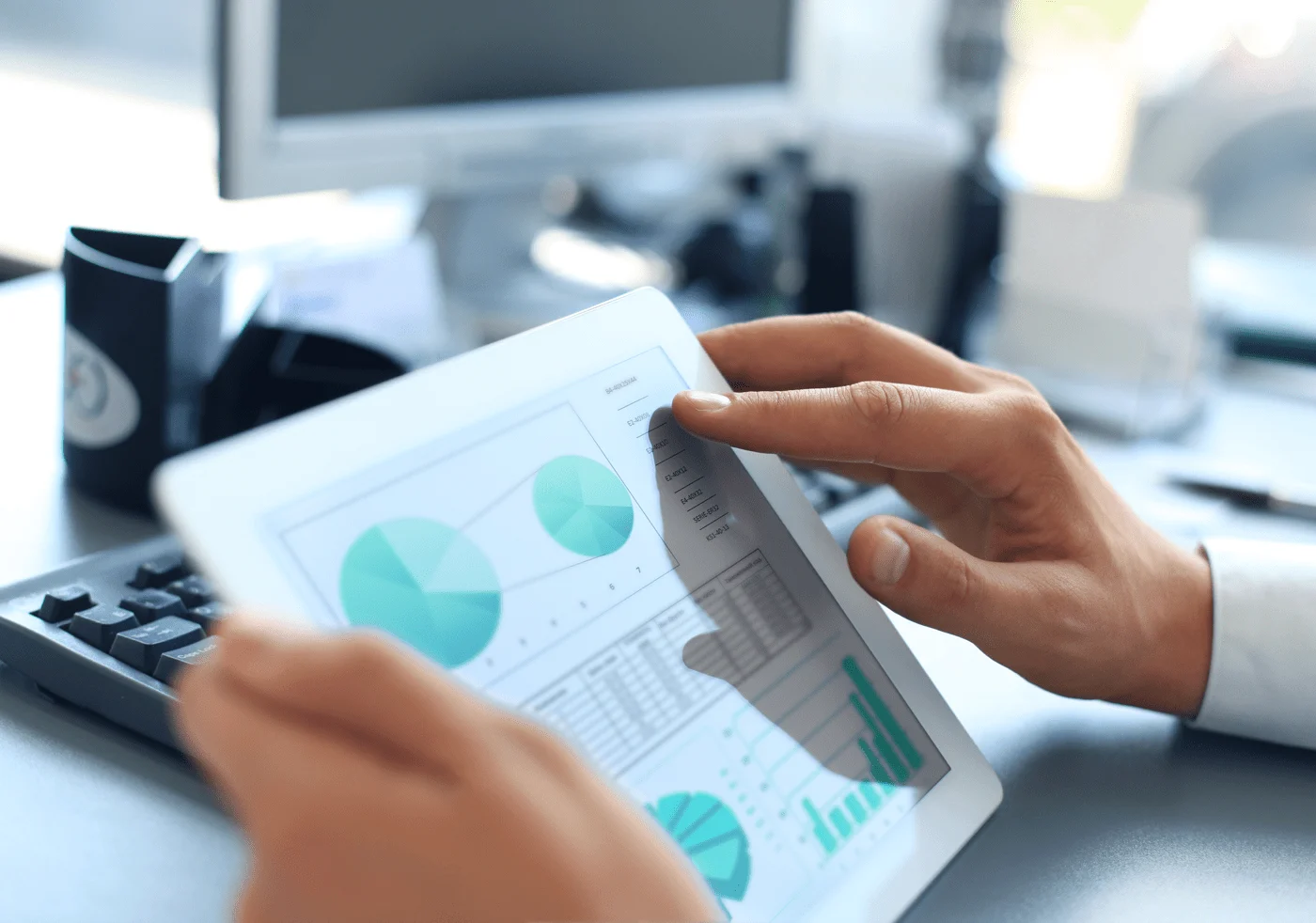 Someone holds a tablet displaying teal data charts.