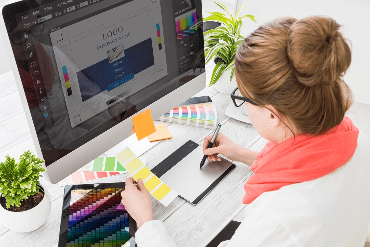 A woman compares color swatches while designing promotional materials.