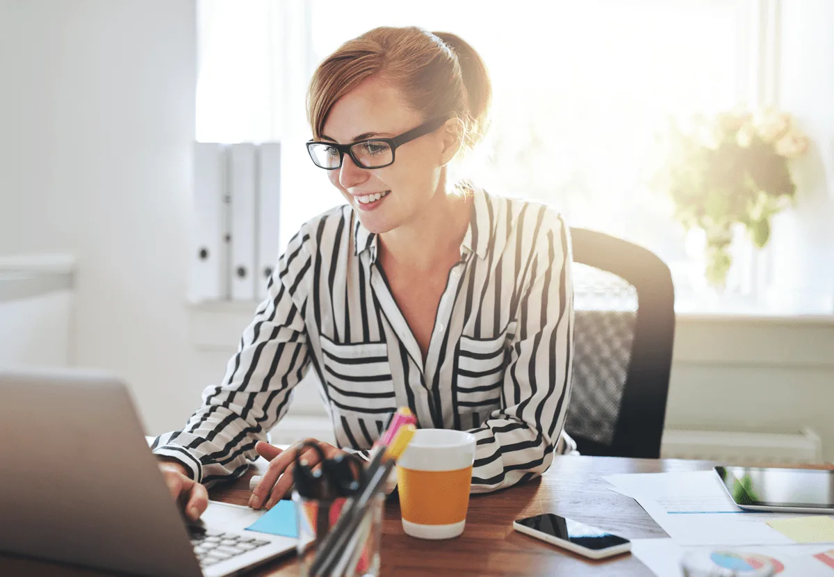 woman smiling at her desk while typing on her laptop