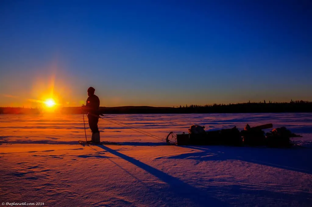 A hiker treks across snow-covered ground, dragging a sled of supplies behind them.