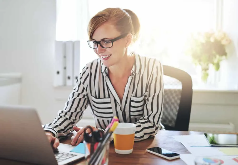 A woman using a laptop computer and drinking coffee.