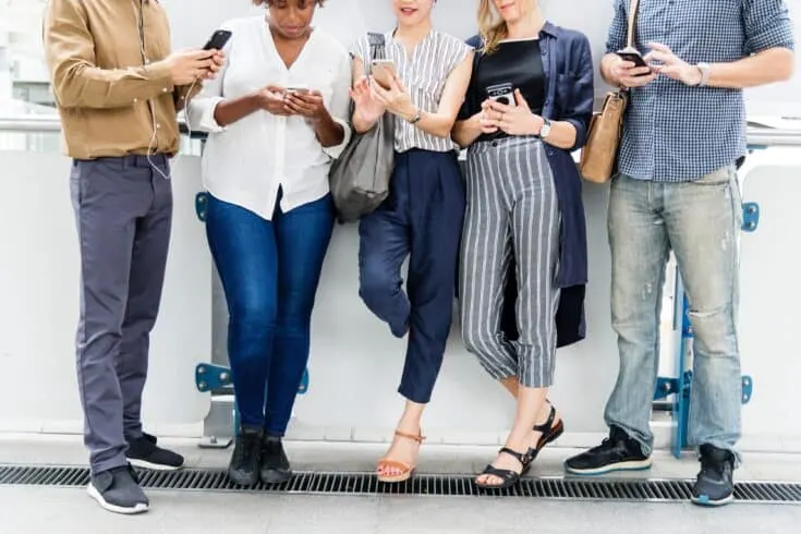 group of people standing against a wall looking at their smartphones