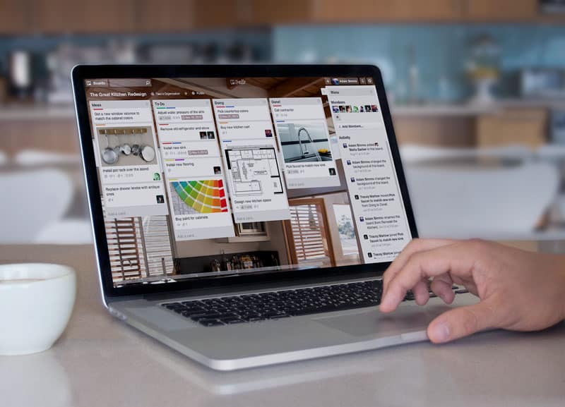 A man using a laptop computer, displaying a Trello board,