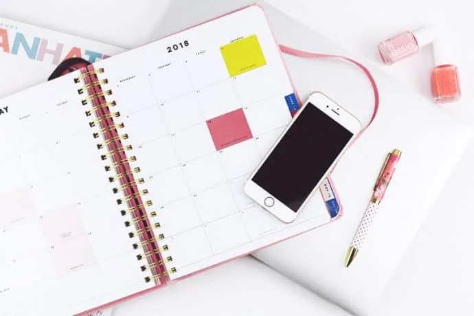 A planner opened to a calendar page, along with a pen, closed laptop computer and smart phone.