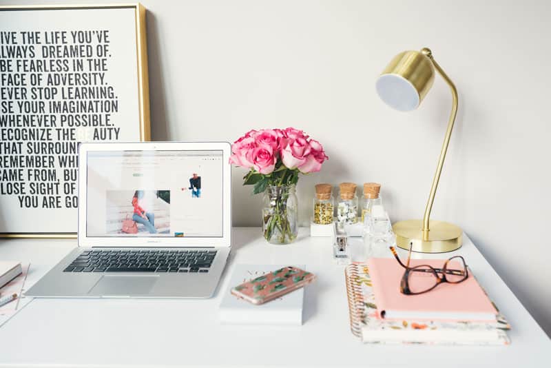 picture of a desk with a laptop, notebooks, gold lamp and a vase of flowers