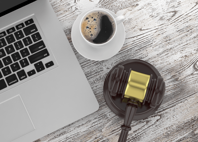 A desktop with a laptop computer, cup of coffee, and a judge's gavel.