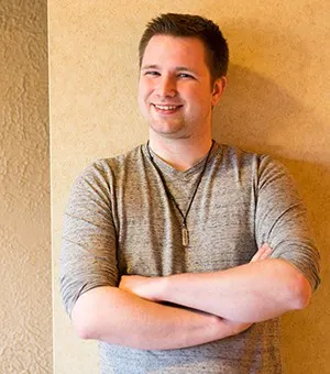 Alex Roth stands against a beige wall, with arms crossed.