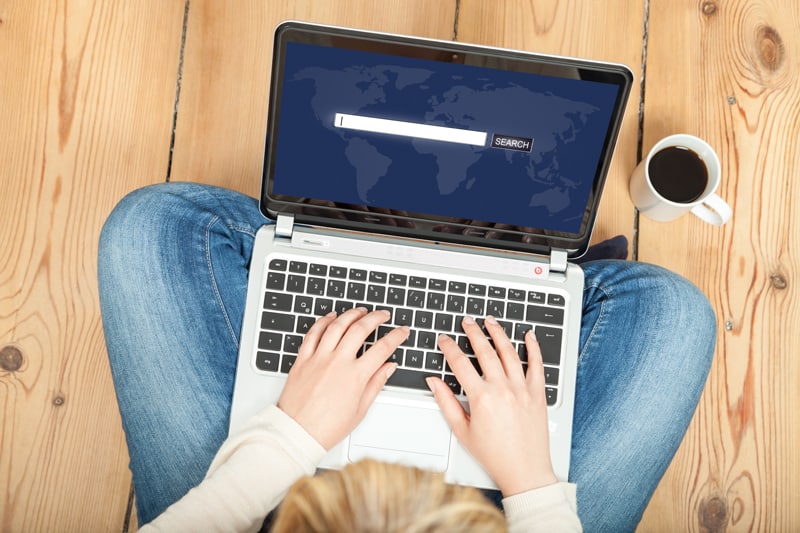 A blogger sits cross legged with a computer in their lap, typing into a search bar.