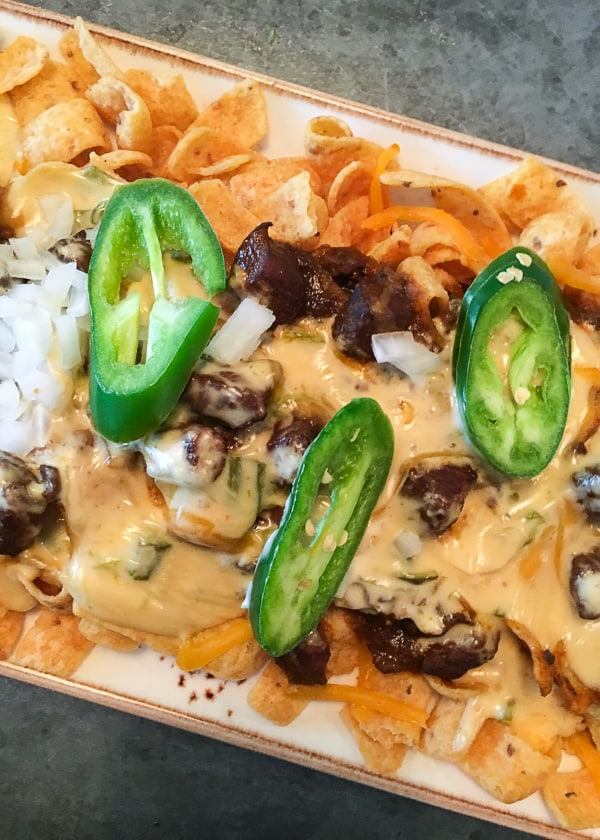 A plate of Frito pie topped with jalapenos, cheese sauce and chopped onion.