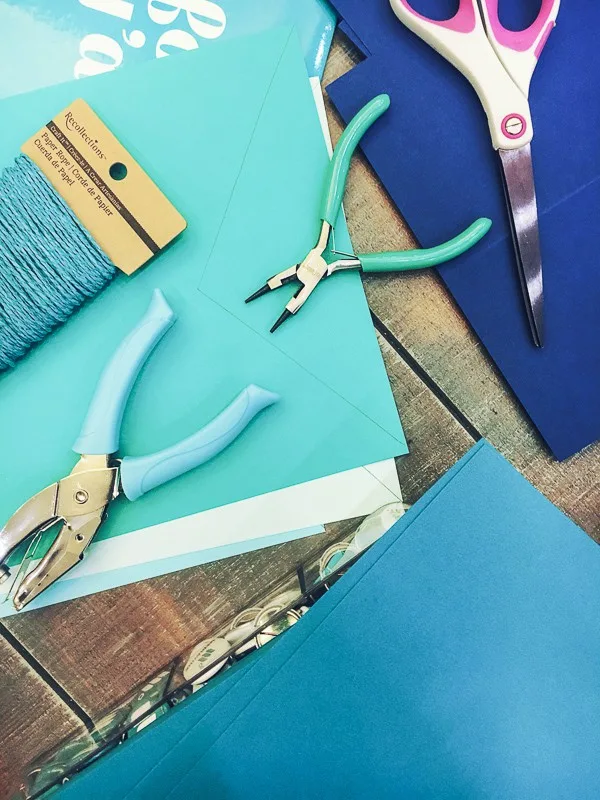 DIY supplies laid out over a table, including tweezers, twine, scissors, paper and a hole punch.