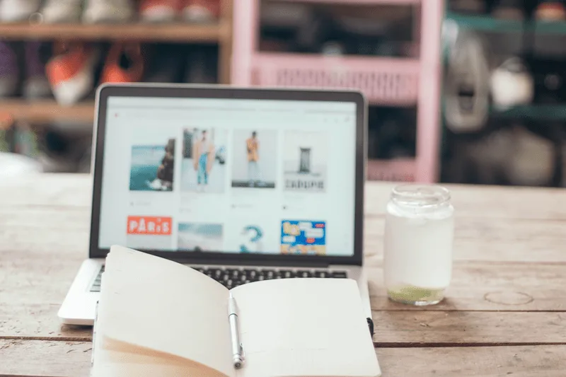 laptop with a Pinterest feed and an empty journal with a pen