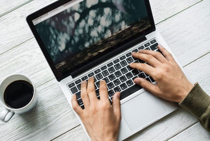 man typing on a laptop with a coffee cup next to him