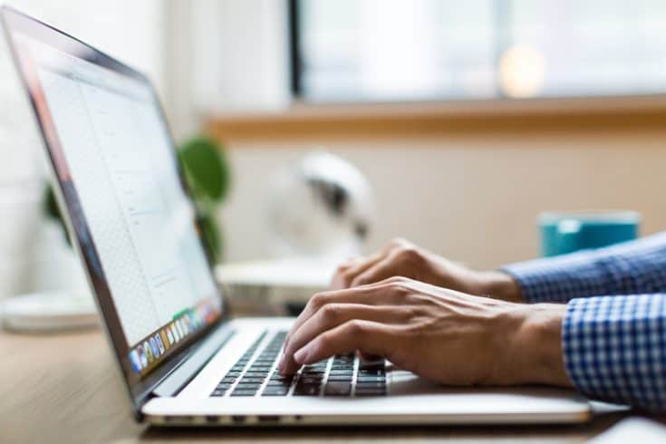 A man's hands typing on a laptop computer.