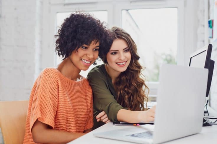 two women smiling while looking at a laptop screen 