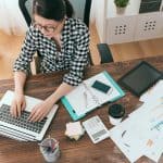 top view of woman typing on laptop with office supplies scattered on table