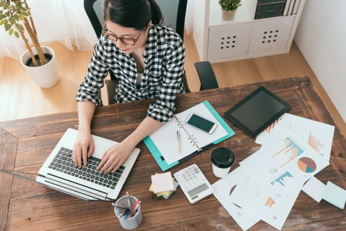 top view of woman typing on laptop with office supplies scattered on table