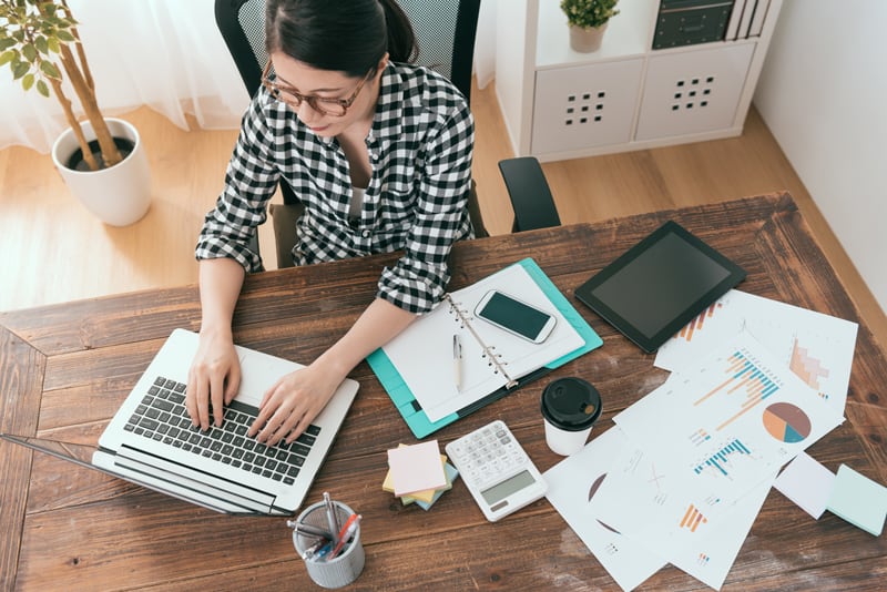 top view of woman typing on laptop with office supplies scattered on table