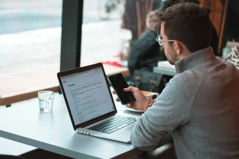 A man using a laptop computer and mobile phone at a cafe.