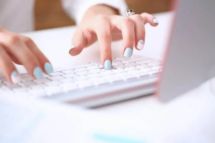 woman's hands with blue and white nails typing on a keyboard