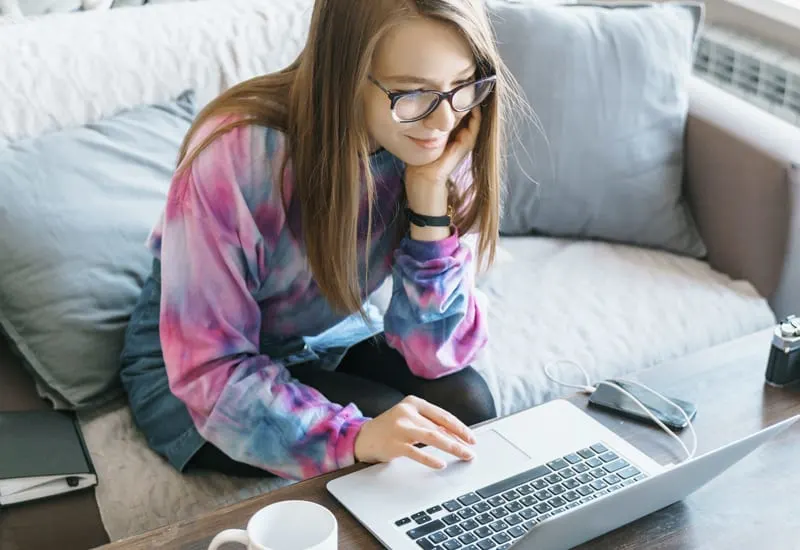 A woman sitting on a love seat and using a laptop computer.