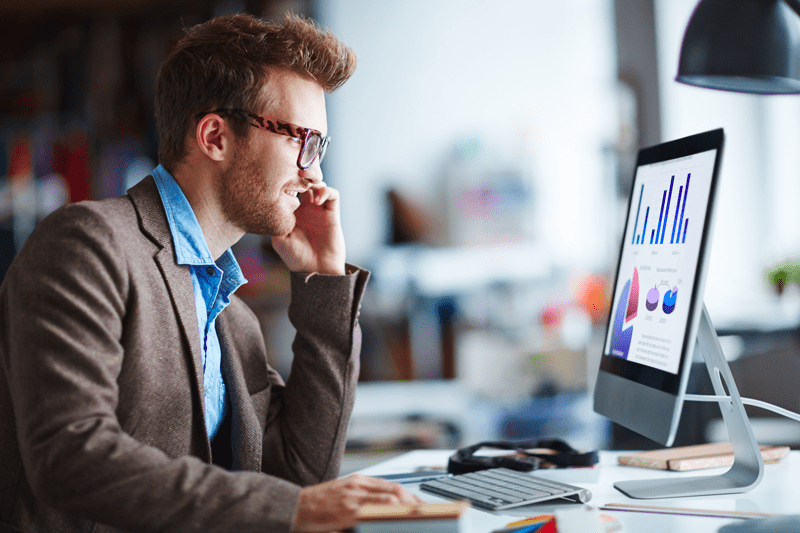 A man looks over graphs and charts on a desktop computer.