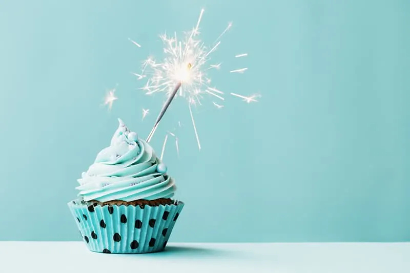 A teal cupcake with a sparkler candle.