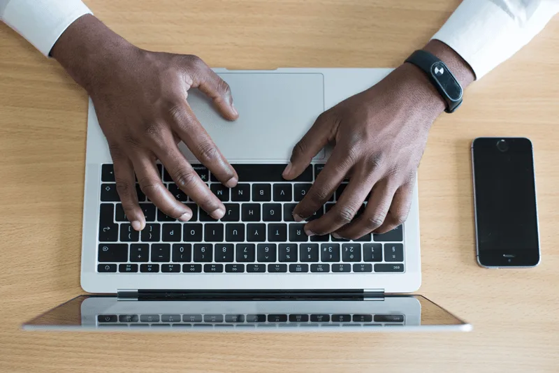 A top-down view of a man's hands typing on a computer.