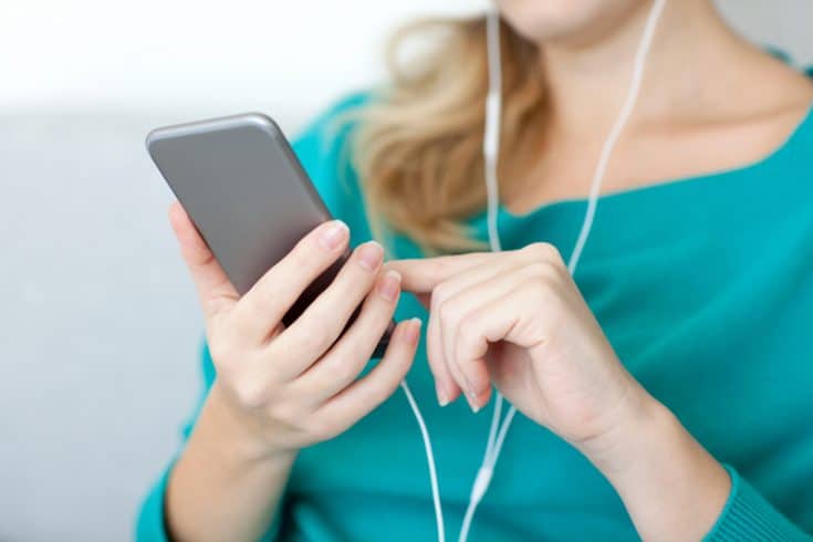 women in teal shirt with earbuds in scrolling on her smartphone