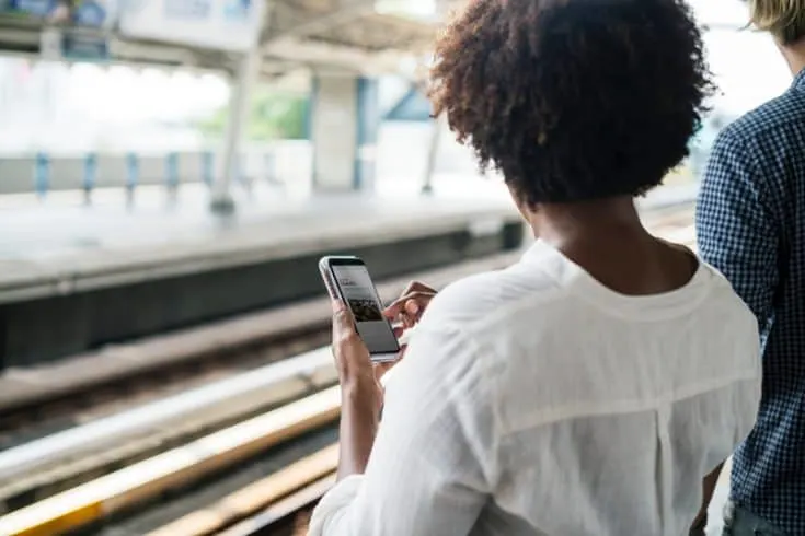 A woman standing in a train station browses the Internet on a smart phone.