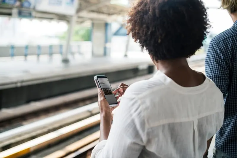 A woman using a smart phone in front of train tracks.