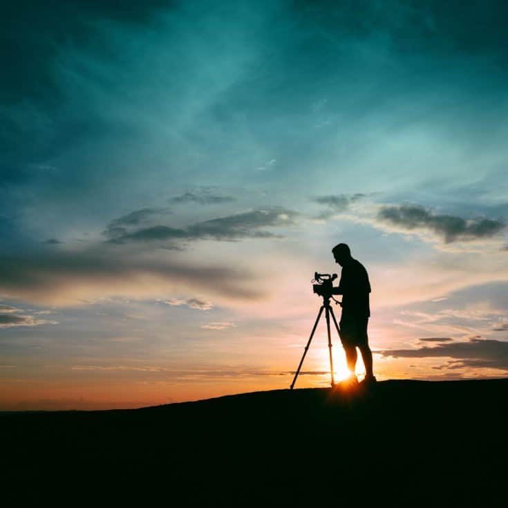 The silhouette of a man filming, while the sun sets behind him.