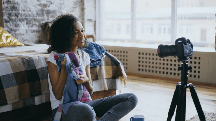 A woman vlogs in a bedroom, showing clothing to the camera.