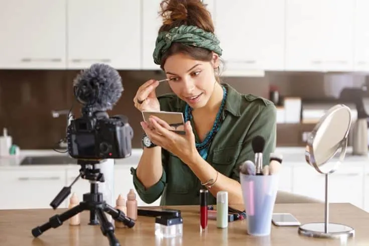 beauty blogger filming herself putting on makeup in a mirror