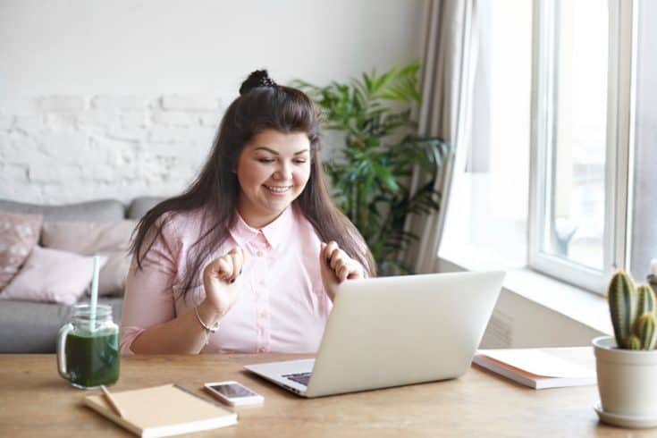 Woman happy with her work on her laptop by a window in her home office
