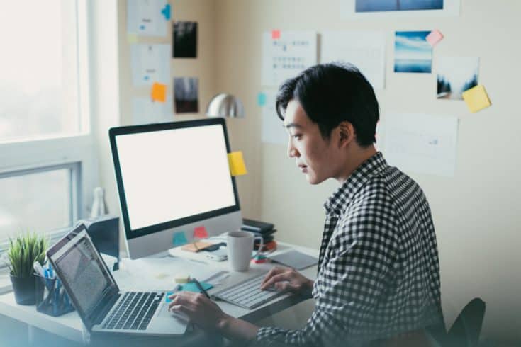 a developer working on a laptop and a desktop computer simultaneously in a home office