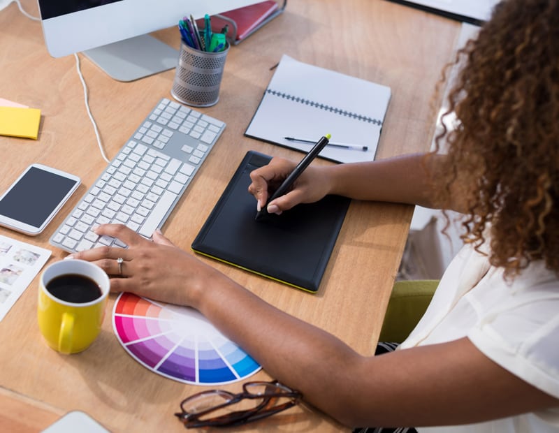 A graphic designer drawing on a tablet while comparing colors to color swatches.