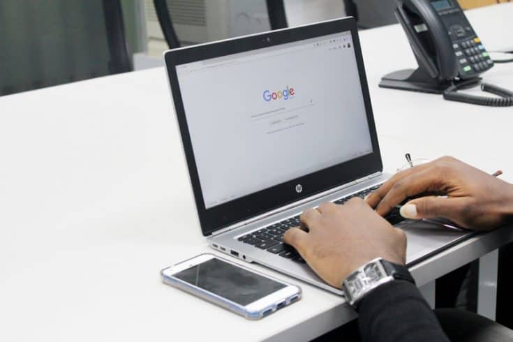 Hands typing at a laptop computer on the Google search homepage.