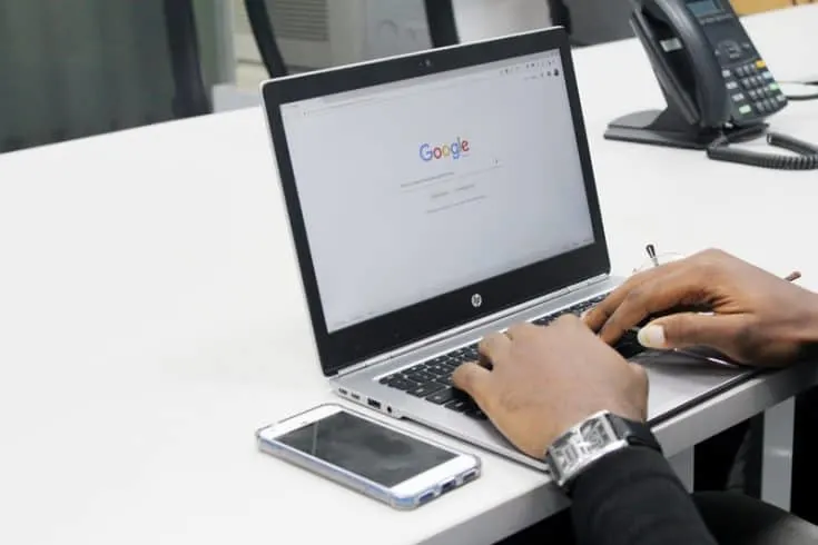 Man typing on laptop computer open to Google search bar home page.