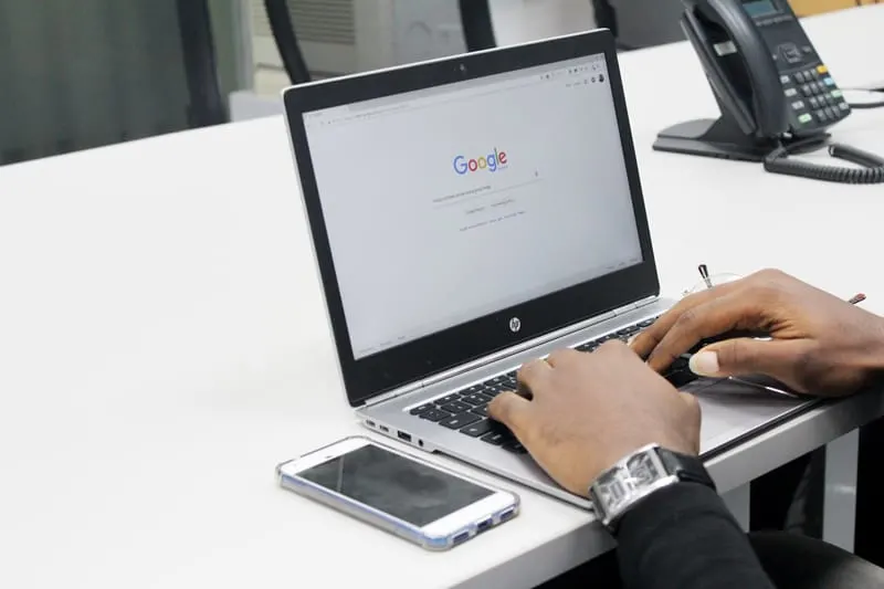 A man types on a laptop computer, currently open to the Google search bar home page.