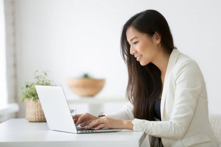 woman sitting at a desk typing a campaign report on a laptop 