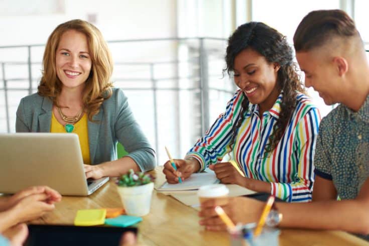 A group of people taking notes in notebooks or on a laptop computer.