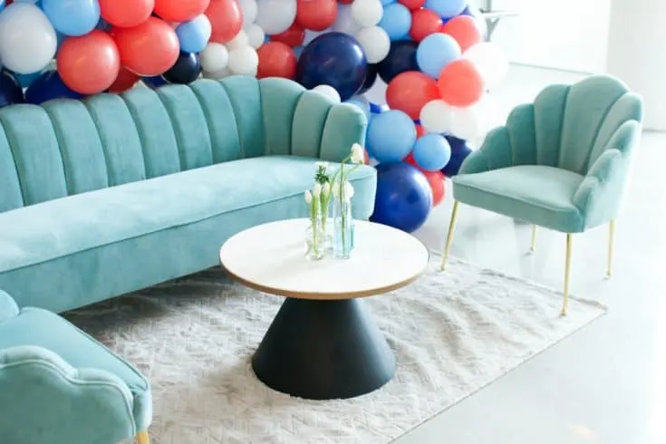 A seating area set up with two chairs, a couch, and coffee table, framed with a balloon arch.